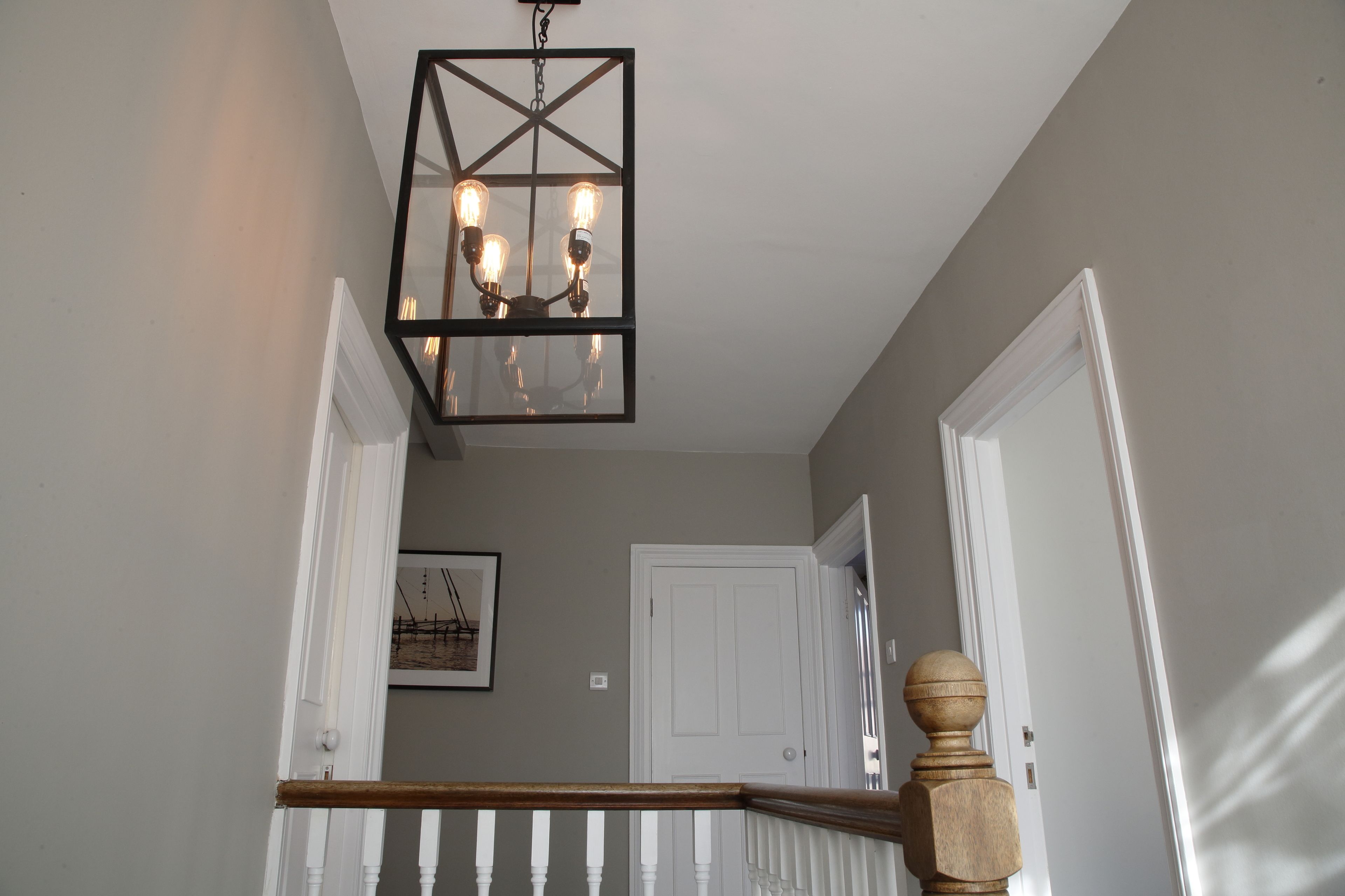 A staircase with a wooden handrail and a black metal chandelier with four bulbs.