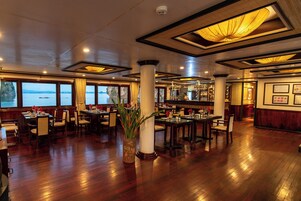 Un restaurante espacioso con suelos de madera, amplias ventanas que ofrecen vistas al agua y una zona de bar con una variedad de botellas.