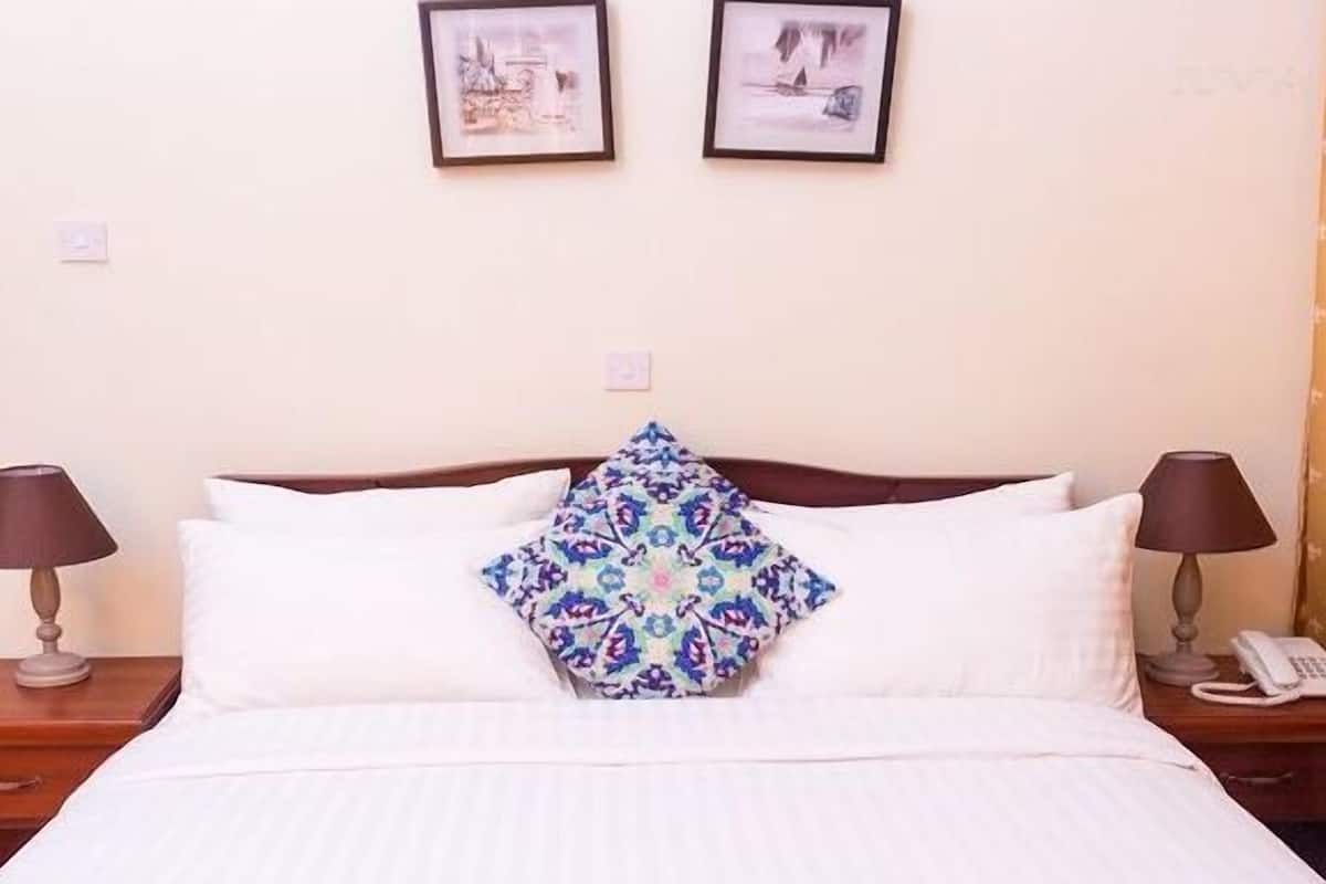 A hotel room with a bed, two bedside lamps, a telephone, and two framed pictures on the wall.