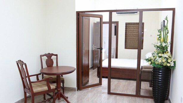 A room with a bed, a wooden chair, a round table, and a large mirror. - Lake Bosumtwi Hotel & Apartments (Accra)