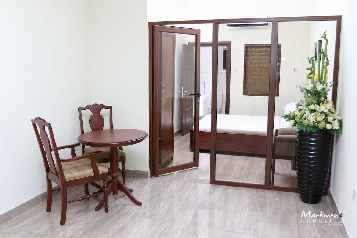 A room with a bed, a wooden chair, a round table, and a large mirror.