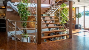 A modern hotel lobby with a curved staircase, wooden paneling, and potted plants. - Select MS Serenity - Neuss (Neuss)