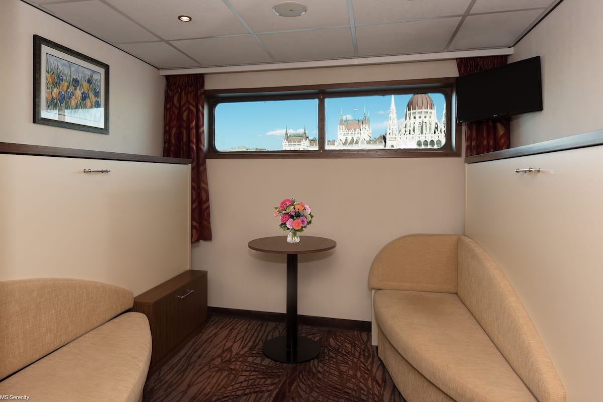 A hotel room with a large window, a small table with a vase of flowers, and two sofas.