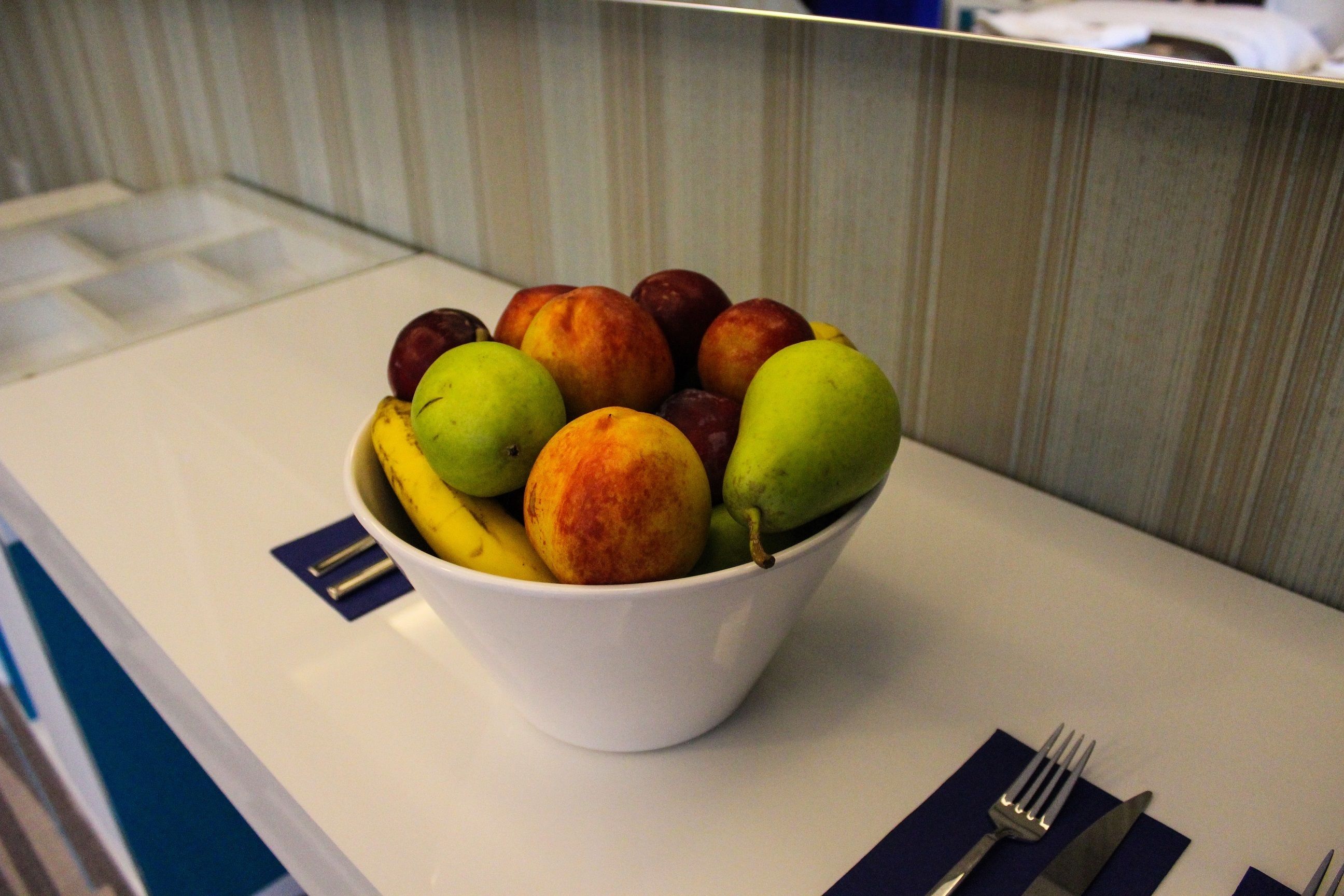 Eine Schüssel Obst auf einem Tisch, daneben ein Messer und eine Gabel.