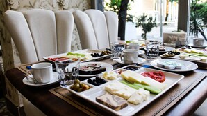 Bandeja de desayuno con varios quesos, aceitunas y frutas sobre una mesa con vistas a un jardín.