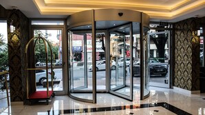 Entrada de hotel con puerta giratoria, alfombra roja y vistas de la calle.