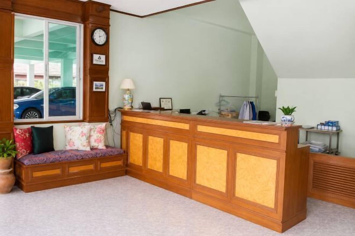 Un espace d’accueil avec un bureau en bois, un banc avec des coussins, une horloge et une fenêtre donnant sur une voiture.