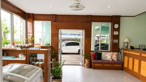 A hotel lobby with a reception desk, a seating area, a large ice cream freezer, and a view of the street. - V.House Nakhon (Nakhon Si Thammarat)