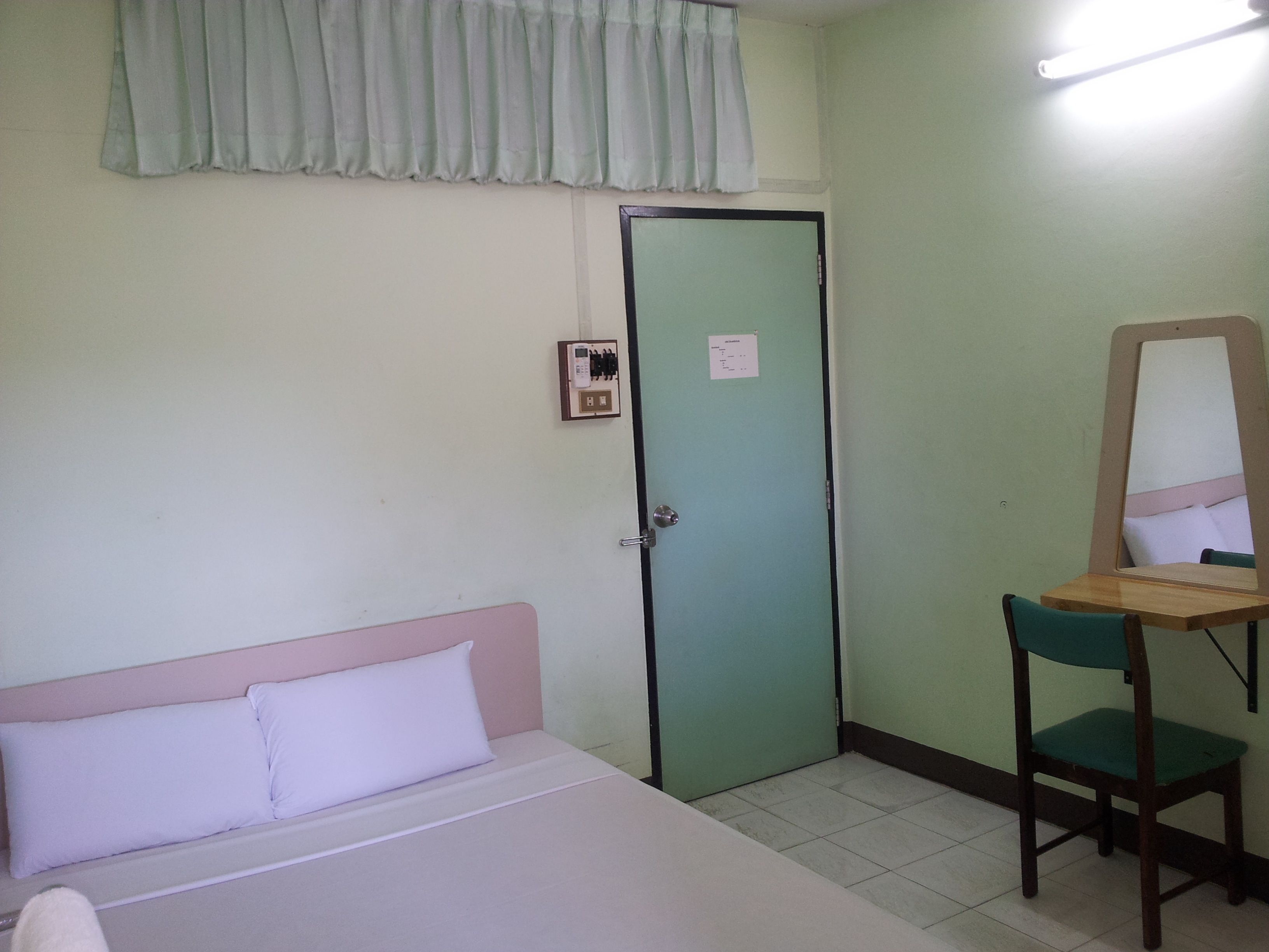 A room with a bed, a green door, a mirror, and a chair.
