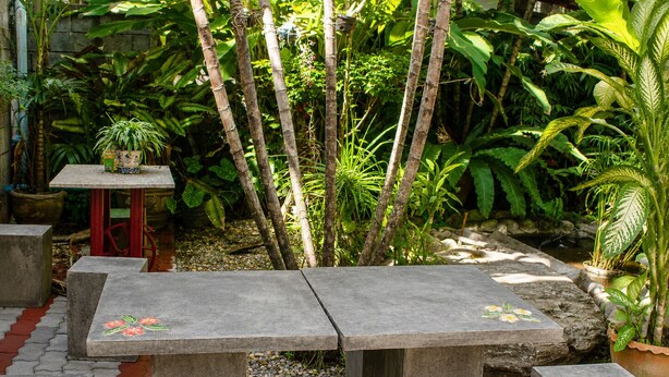 A garden with stone tables and benches, surrounded by lush greenery and potted plants. - V.House Nakhon (Nakhon Si Thammarat)