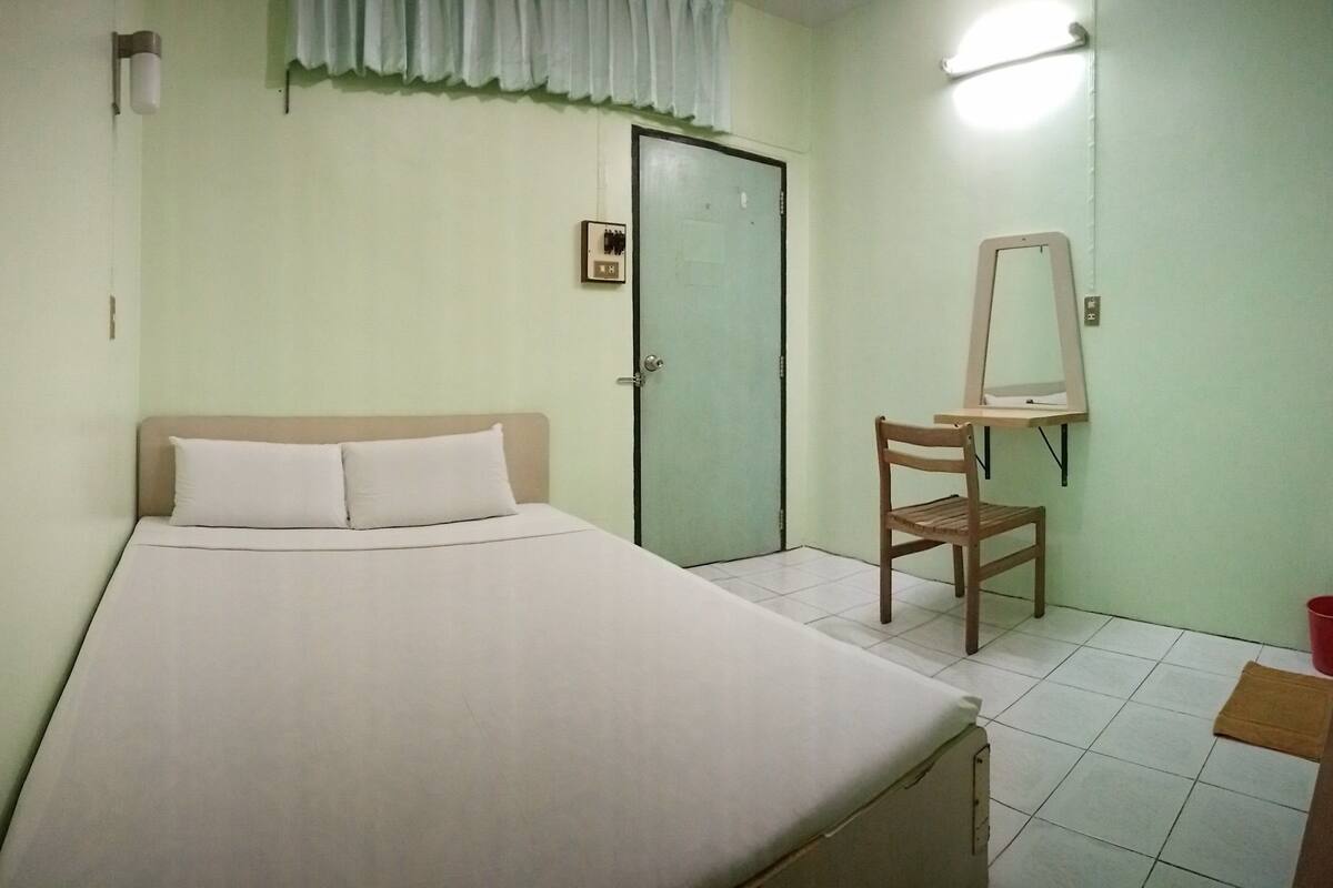 Une pièce simple et dépouillée, avec un lit, une chaise, une porte et un miroir.