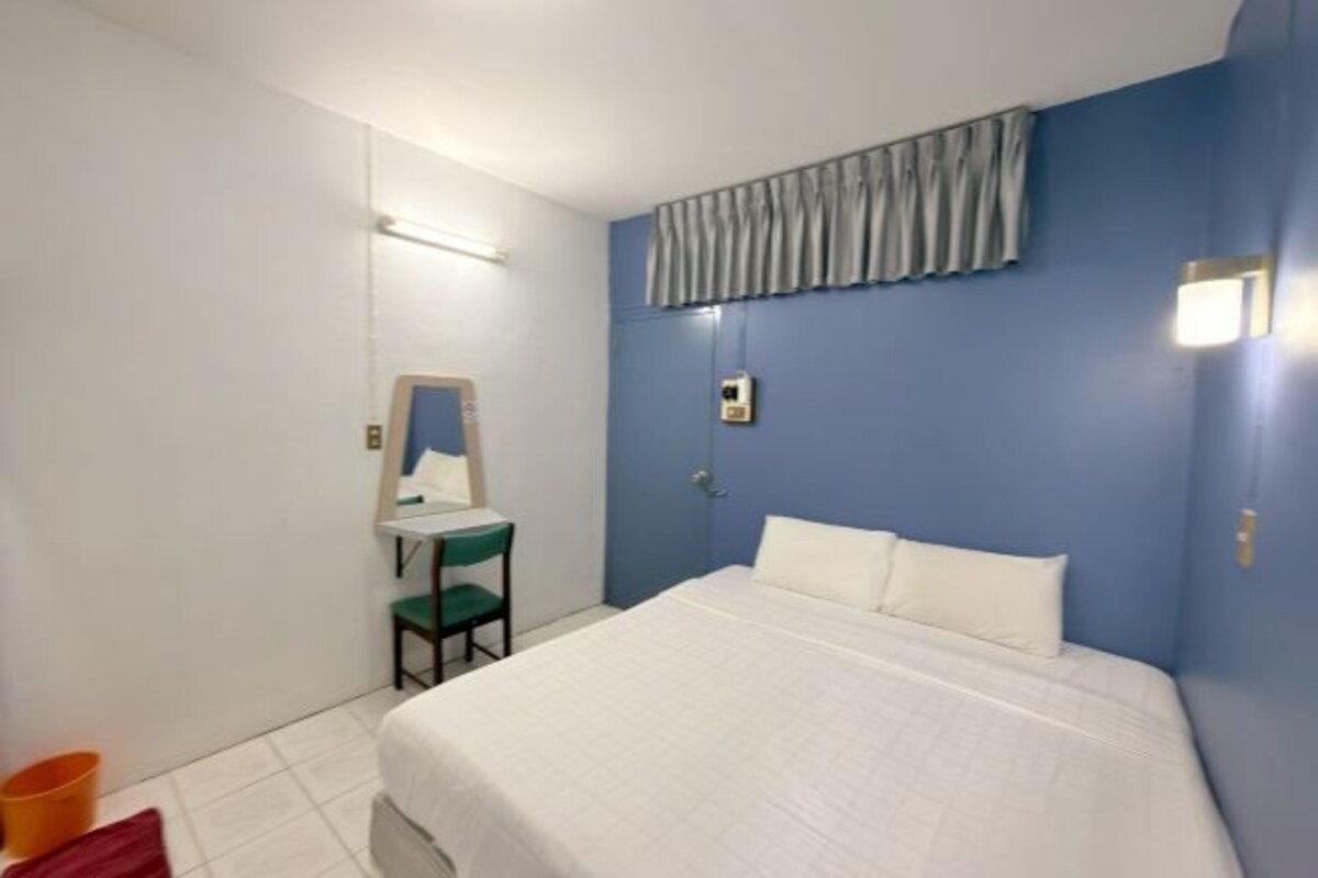 Un dormitorio con cama, una silla, un espejo, una mesita de noche y un aplique de pared.