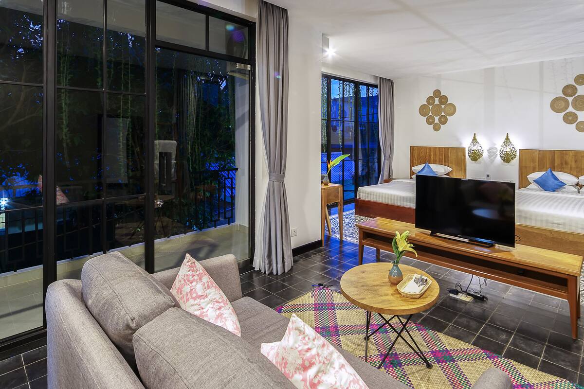 A modern hotel room with a large window, a sofa, a TV, a bed with blue pillows, and decorative wall art.