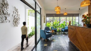 A modern reception area with a wooden reception desk, blue chairs, and a large window with plants. - VIHARA The City of Temples (Siem Reap)
