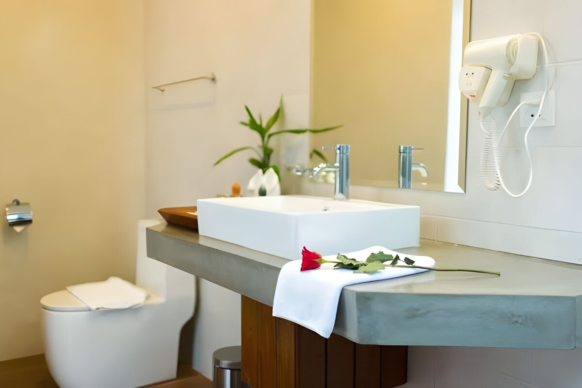 Un baño con lavamanos blanco, espejo, secador de pelo, inodoro y una planta en maceta.