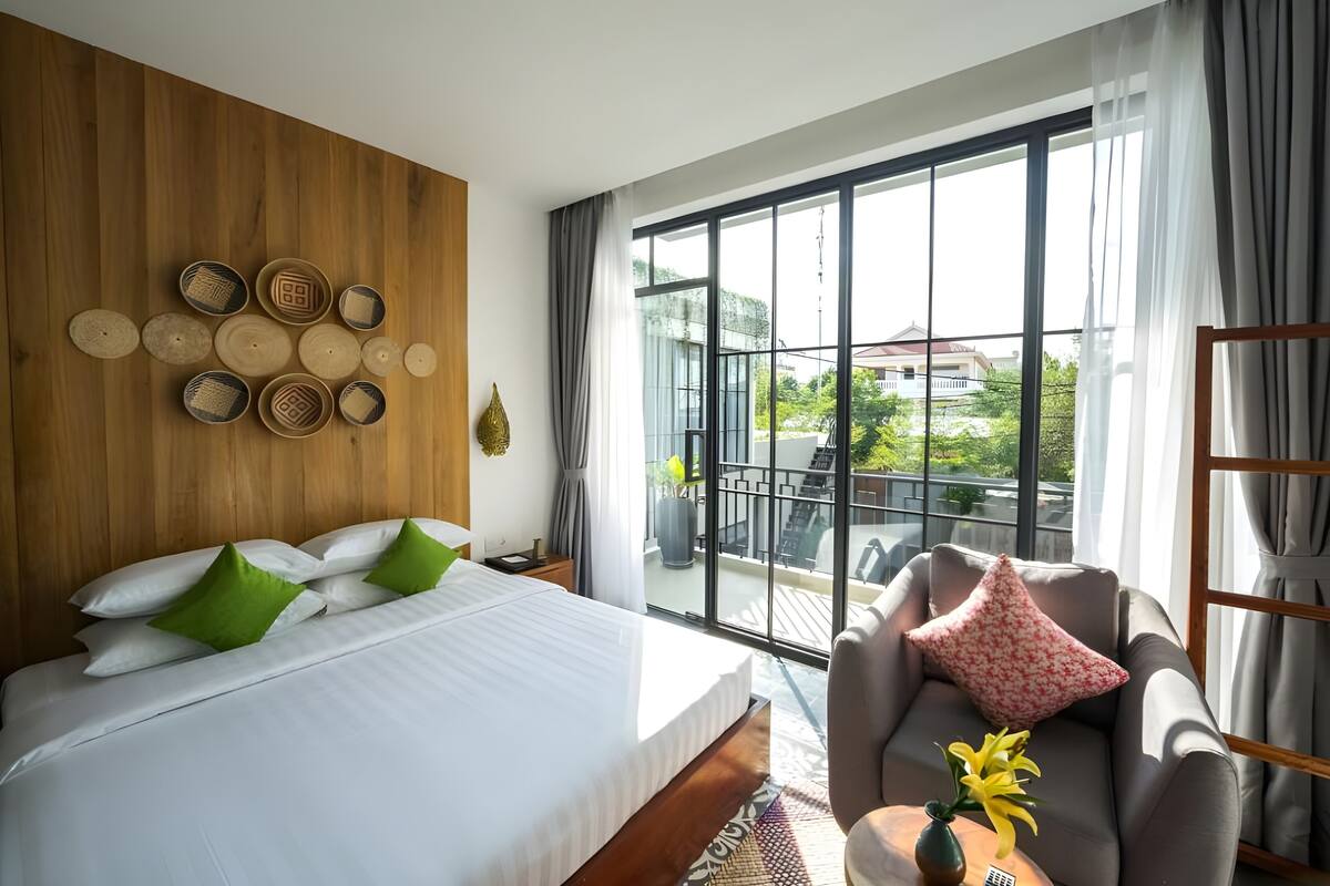 A bedroom with a large bed, a sofa, and a view of a balcony with outdoor furniture.