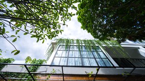 A modern building with large windows and a view of the sky through the foliage. - VIHARA The City of Temples (Siem Reap)
