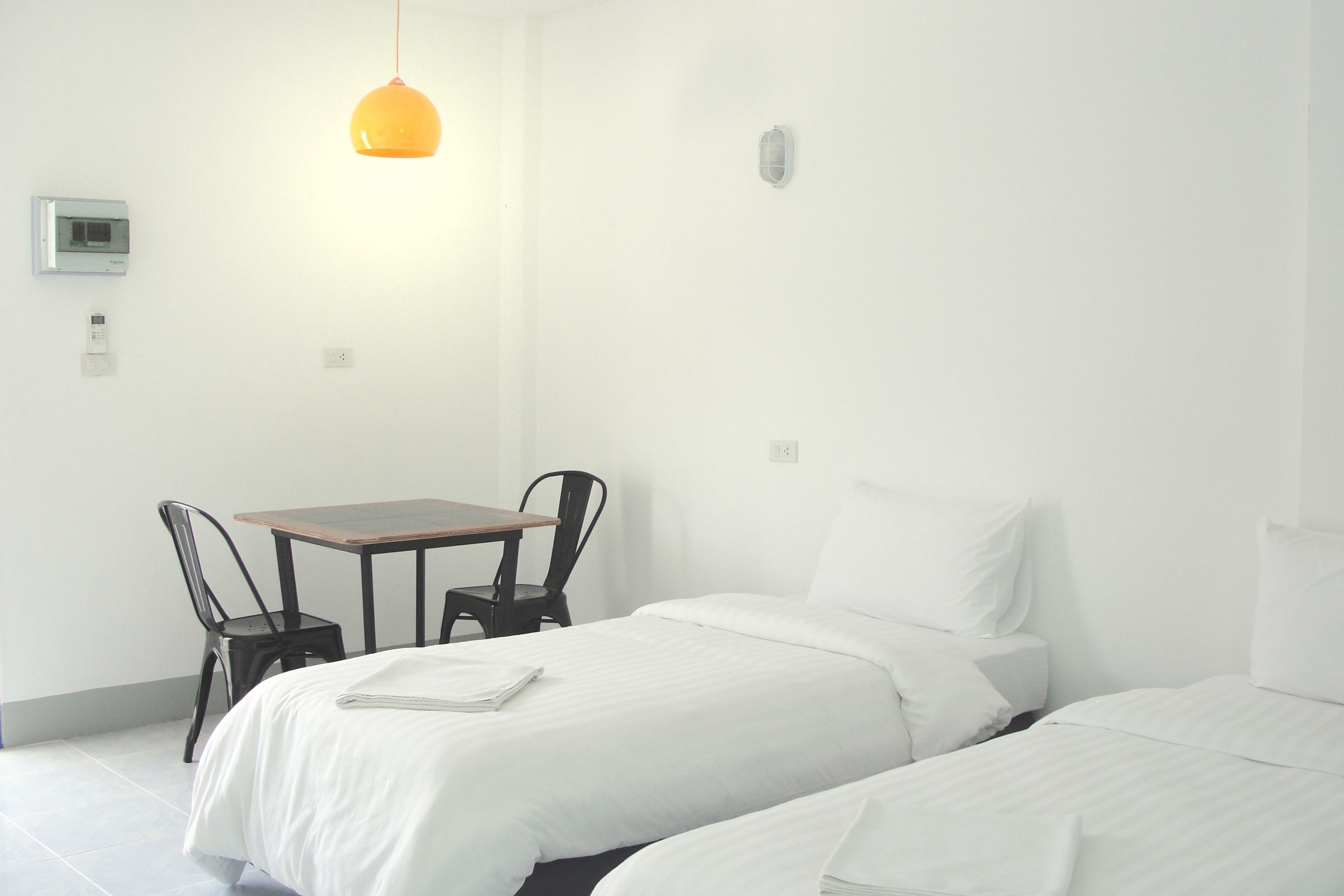 A hotel room with two beds, a small table, two chairs, a hanging light fixture, and a wall-mounted thermostat.