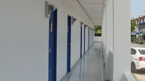 A long, narrow corridor with blue doors on one side and a white wall on the other. - Blue Hip Apartment Nakhon Sri (Nakhon Si Thammarat)