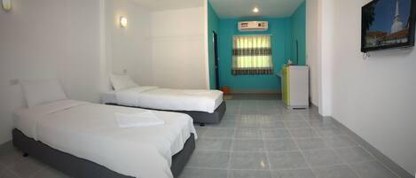 A hotel room with two beds, a small kitchenette, a window with curtains, and a wall-mounted TV.