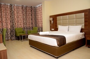 A hotel room with a large bed, a wooden headboard, a green chair, and patterned curtains. - Blu Sky Hotel (Maputo)