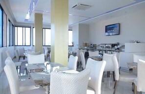 A modern dining area with white furniture and a kitchen in the background. - Blu Sky Hotel (Maputo)