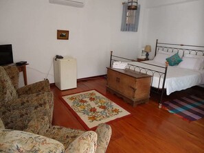 Una camera da letto con un letto, un baule di legno, un piccolo frigorifero, una televisione e un tappeto floreale.