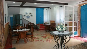A dining area with wooden tables and chairs, a decorative rug, and a central table with a vase of flowers. - Pousada Richard Rothe (Tiradentes)