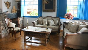 A room with a wooden coffee table, two sofas, a chair, and a window with blue shutters. - Pousada Richard Rothe (Tiradentes)