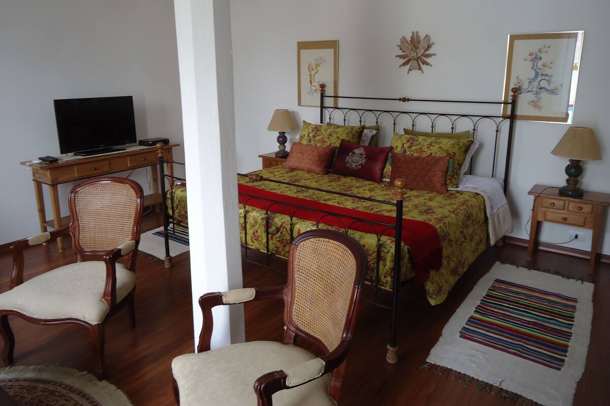 A bedroom with a bed, two chairs, a desk with a computer, and a TV.