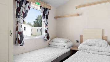 A bedroom with two beds, a window with curtains, a headboard, and a wooden shelf.