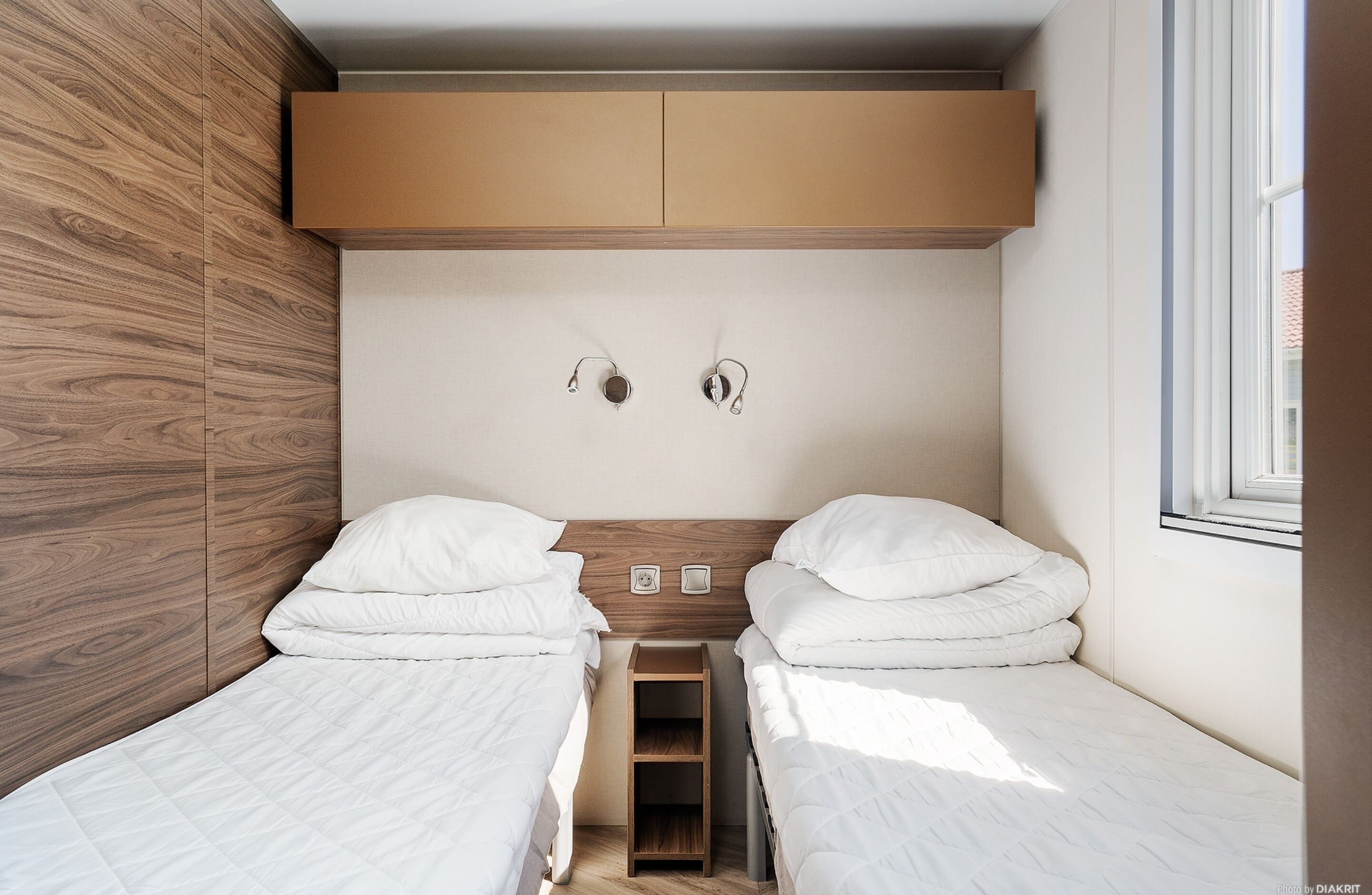 Una camera da letto moderna con due letti singoli, una testiera in legno, un comodino e una finestra.