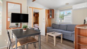 Een ruimtelijk ingerichte leefruimte met een eettafel, bank, televisie en een kleine kitchenette.