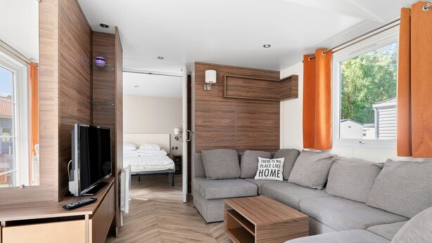 Een moderne woonkamer met een grijze bank, een houten tv-meubel en een flatscreen televisie.
