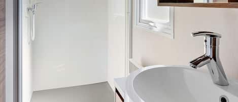A modern bathroom with a white sink, chrome faucet, and a glass shower enclosure.