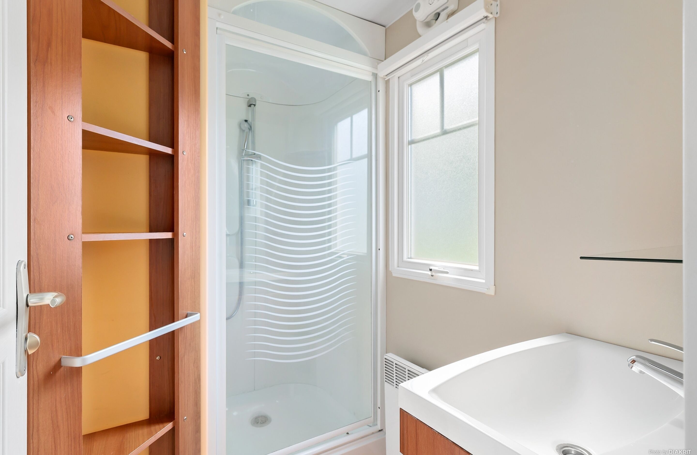 A bathroom with a glass shower enclosure, a white bathtub, and wooden shelving.