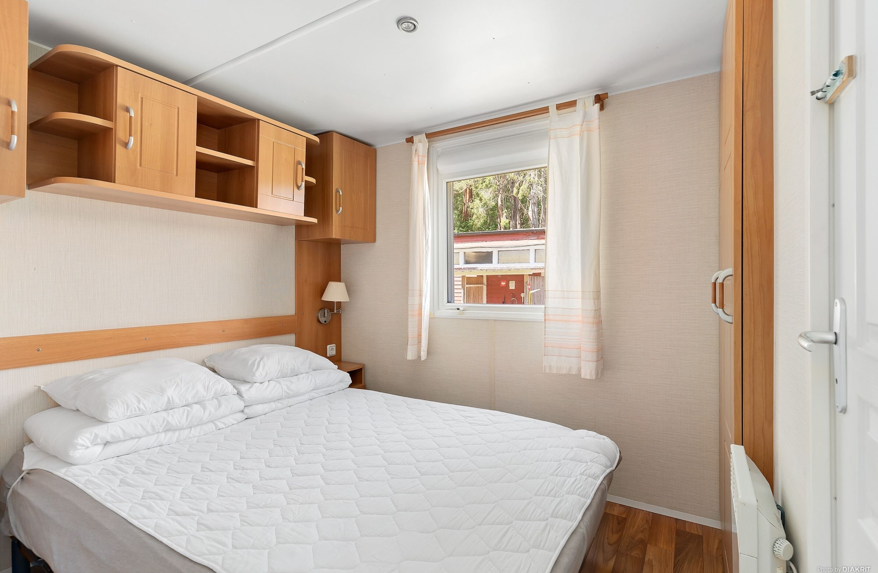 A bedroom with a bed, wooden cabinets, a window with curtains, and a radiator.