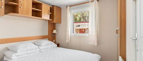 A bedroom with a bed, wooden cabinets, a window with curtains, and a radiator.