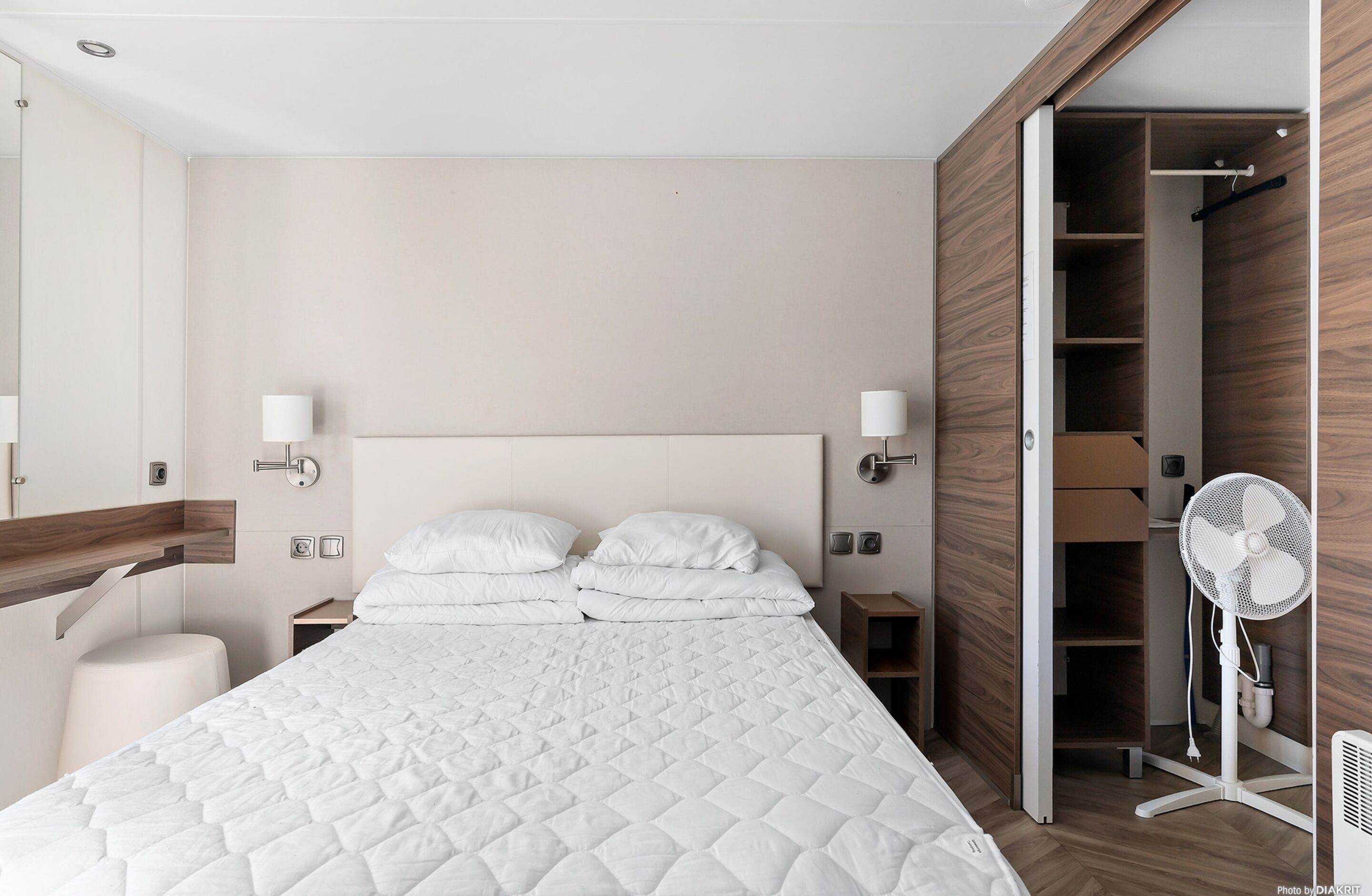 Une chambre d’hôtel moderne avec un grand lit, des lampes de chevet, une armoire et un ventilateur sur pied.