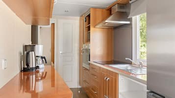 Una cocina compacta con armarios de madera, un refrigerador de acero inoxidable, una cafetera y una ventana que proporciona luz natural.