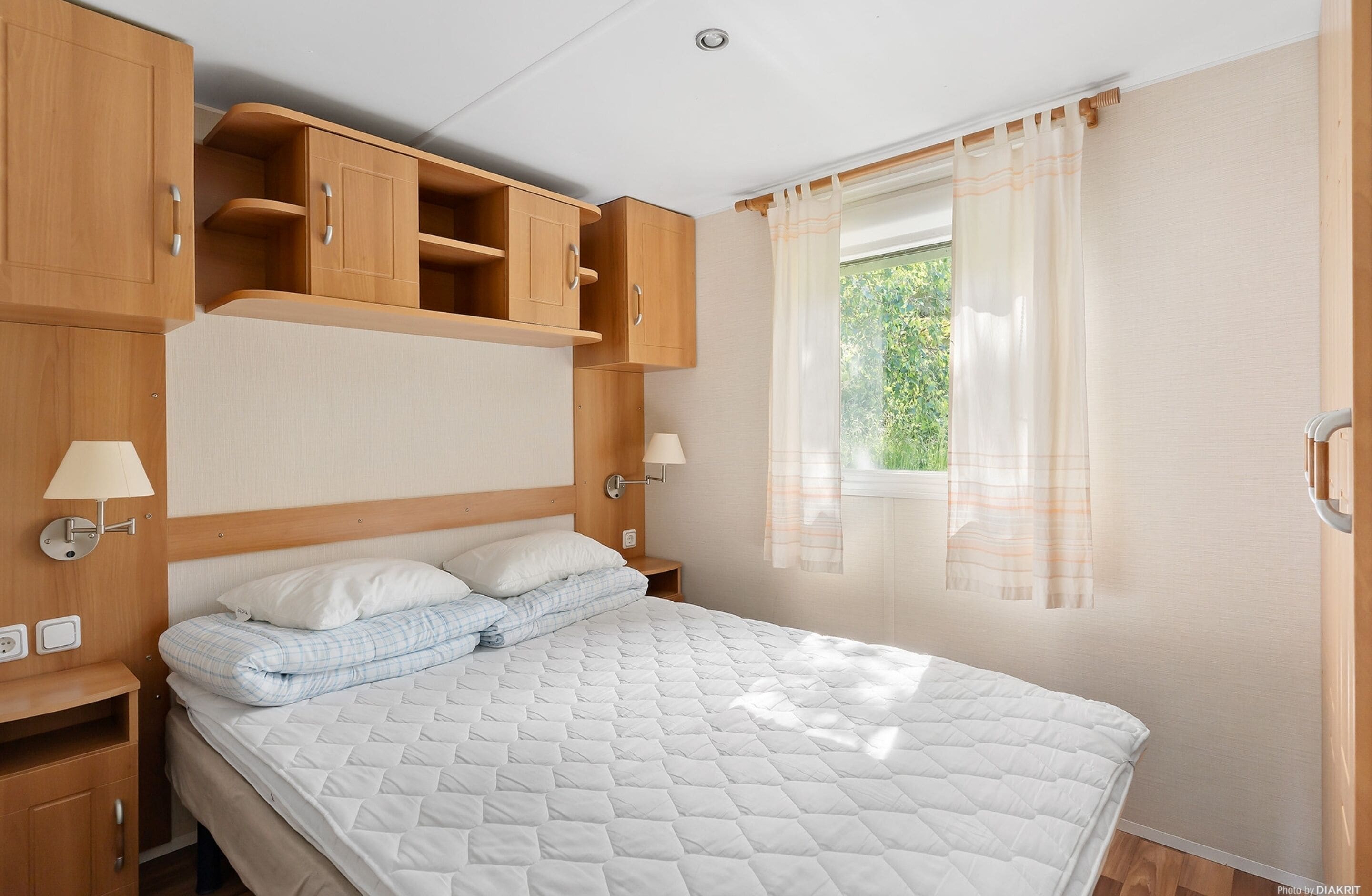 Een slaapkamer met een bed, houten kasten, een nachtkastje en een raam met gordijnen.
