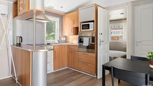 Een kleine keuken met houten kastjes, een ingebouwde magnetron en een roestvrijstalen koelkast.