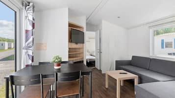 Una habitación moderna y luminosa con una mesa de comedor, sillas, un sofá y un televisor montado en la pared.