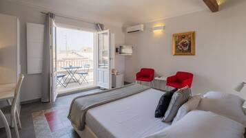 A hotel room with a bed, a red chair, a small table, and a balcony with a view.