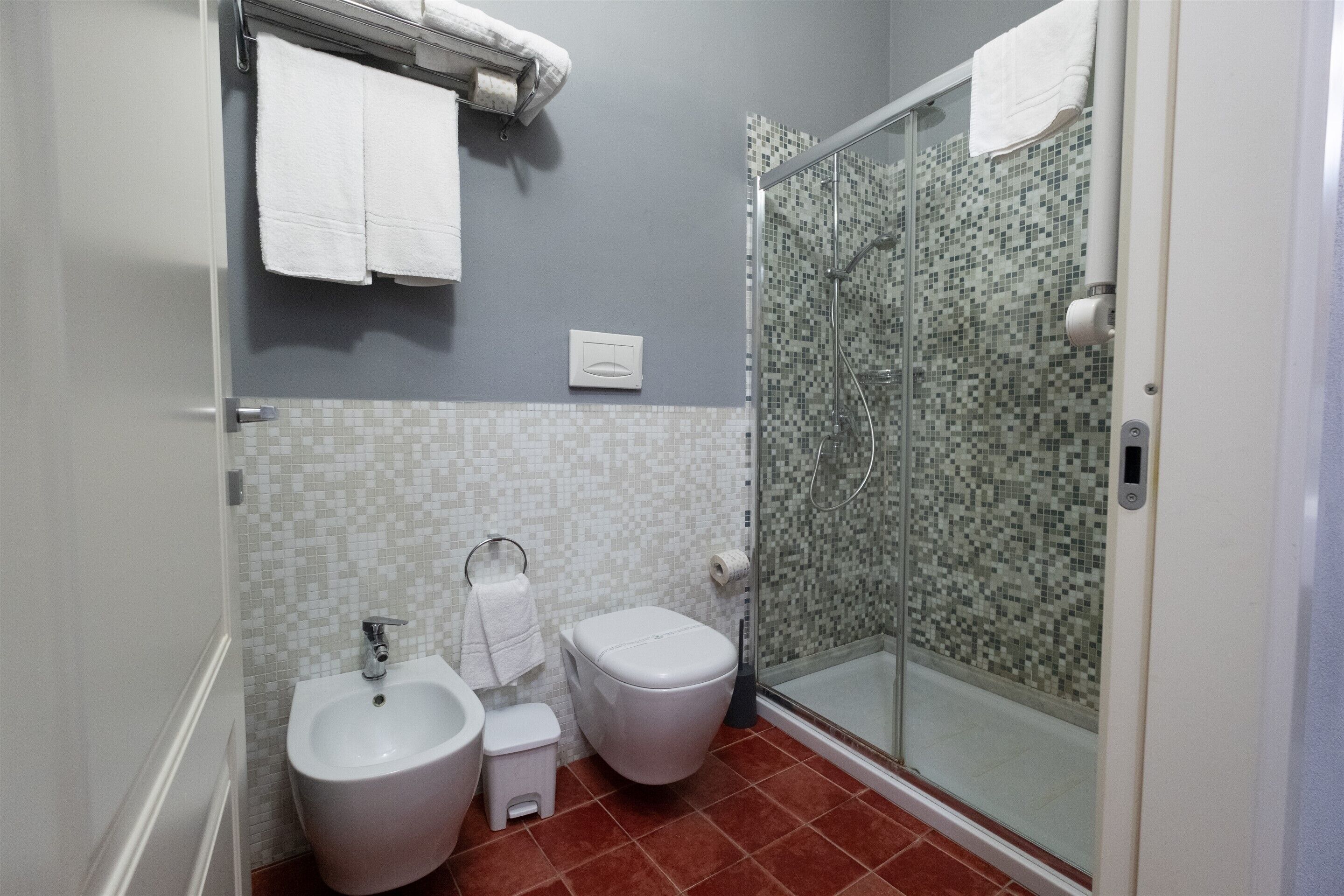 Une salle de bain équipée d’un bidet, de toilettes et d’une douche à parois de verre.