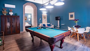 A pool table in a room with blue walls, a wooden cabinet, and a seating area with chairs and a sofa. - Palazzo Gilistro (Syracuse)