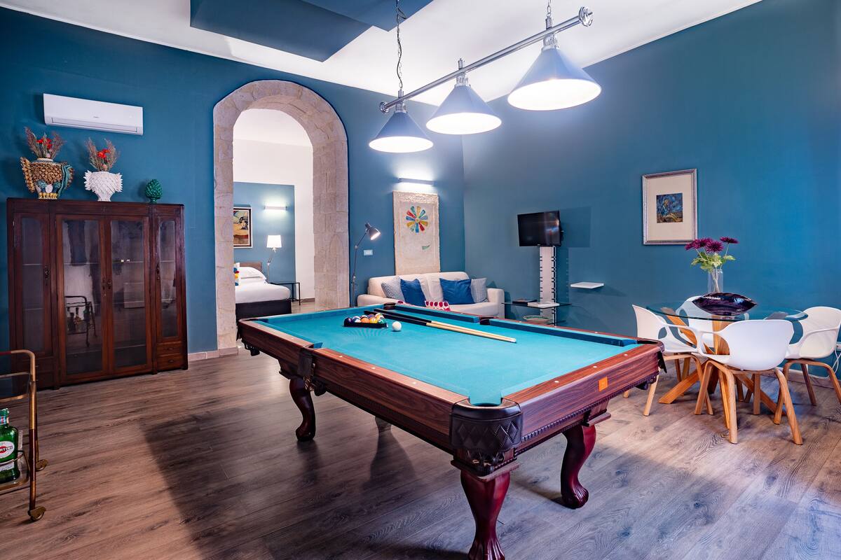 A pool table in a room with blue walls, a wooden cabinet, and a seating area with chairs and a sofa.