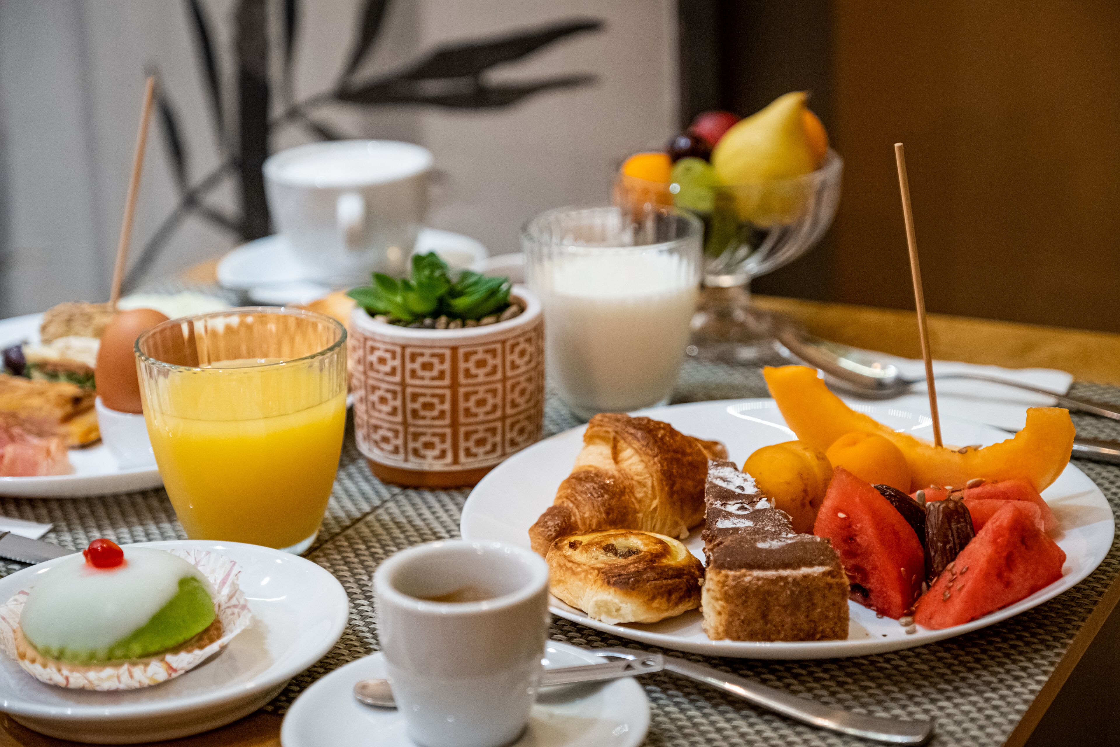 A breakfast setting with various food items, a glass of orange juice, a cup of coffee, and a fruit bowl.