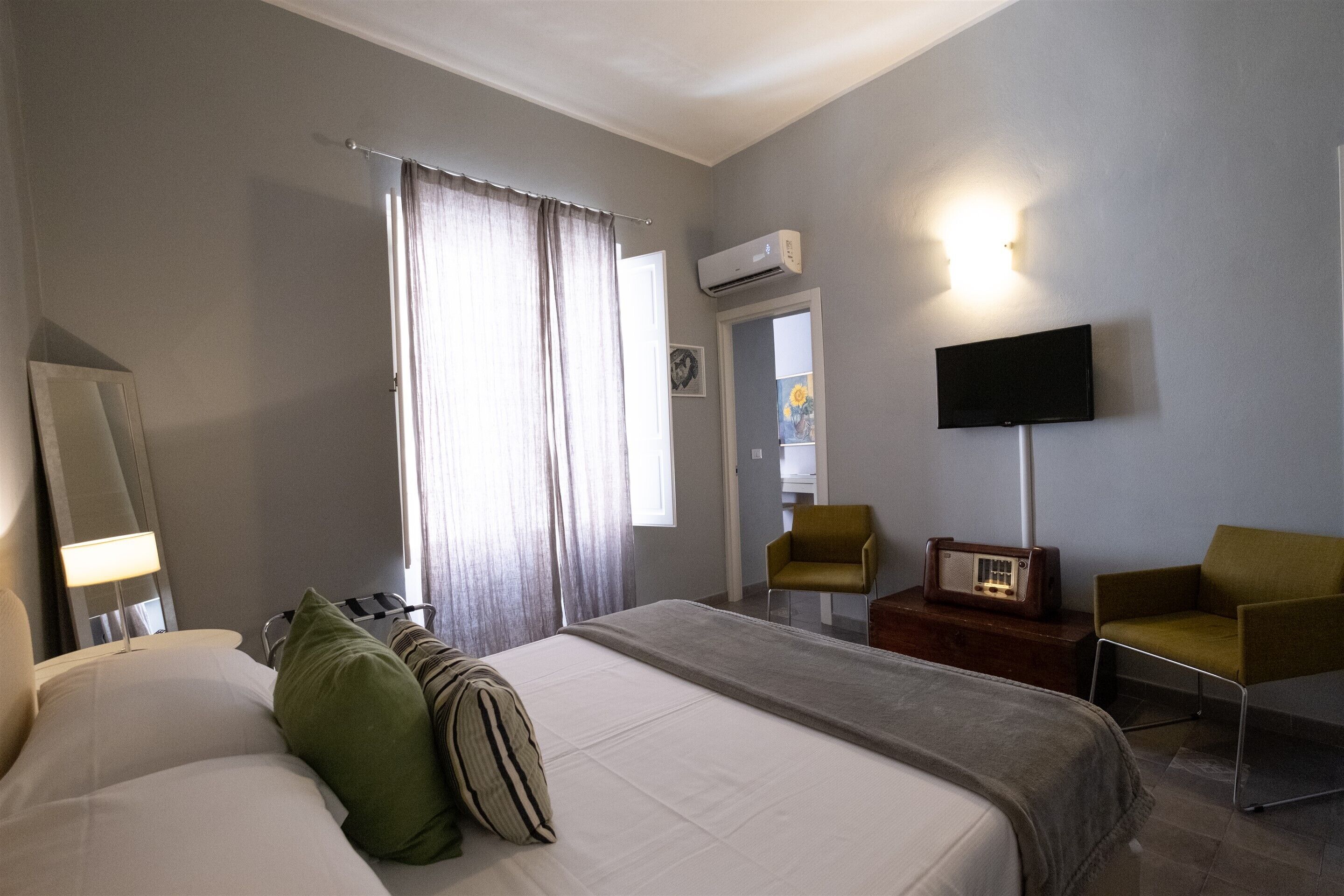 A hotel room with a bed, a chair, a TV, and an air conditioning unit.