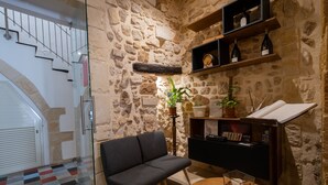 A cozy room with a stone wall, a sofa, a small round table, and a bookshelf with wine bottles. - Palazzo Gilistro (Syracuse)